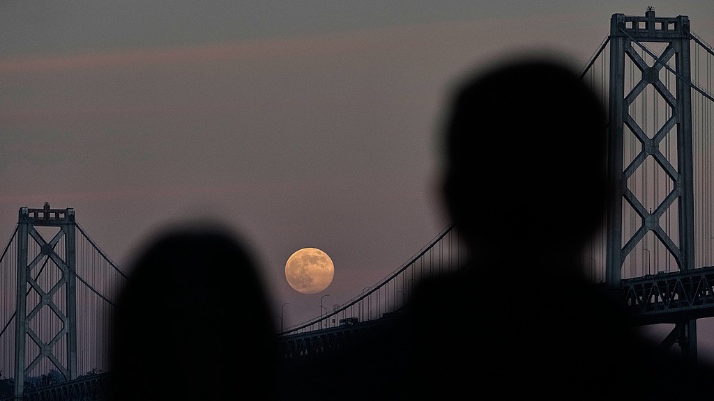 People watch as a supermoon rises behind the San Francisco-Oakland Bay Bridge, U.S., December 4, 2025. /VCG