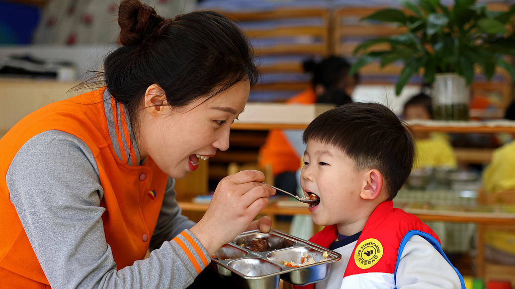 A teacher feeding lunch to a child at a kindergarten in Zaozhuang, Shandong Province, China, November 5, 2025. /VCG
