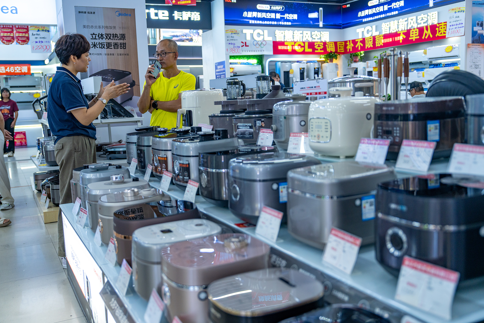 A sales representative explaining to a customer in the home appliances section of a marketplace in Jinhua City, China's Zhejiang Province, August 30, 2025. /VCG
