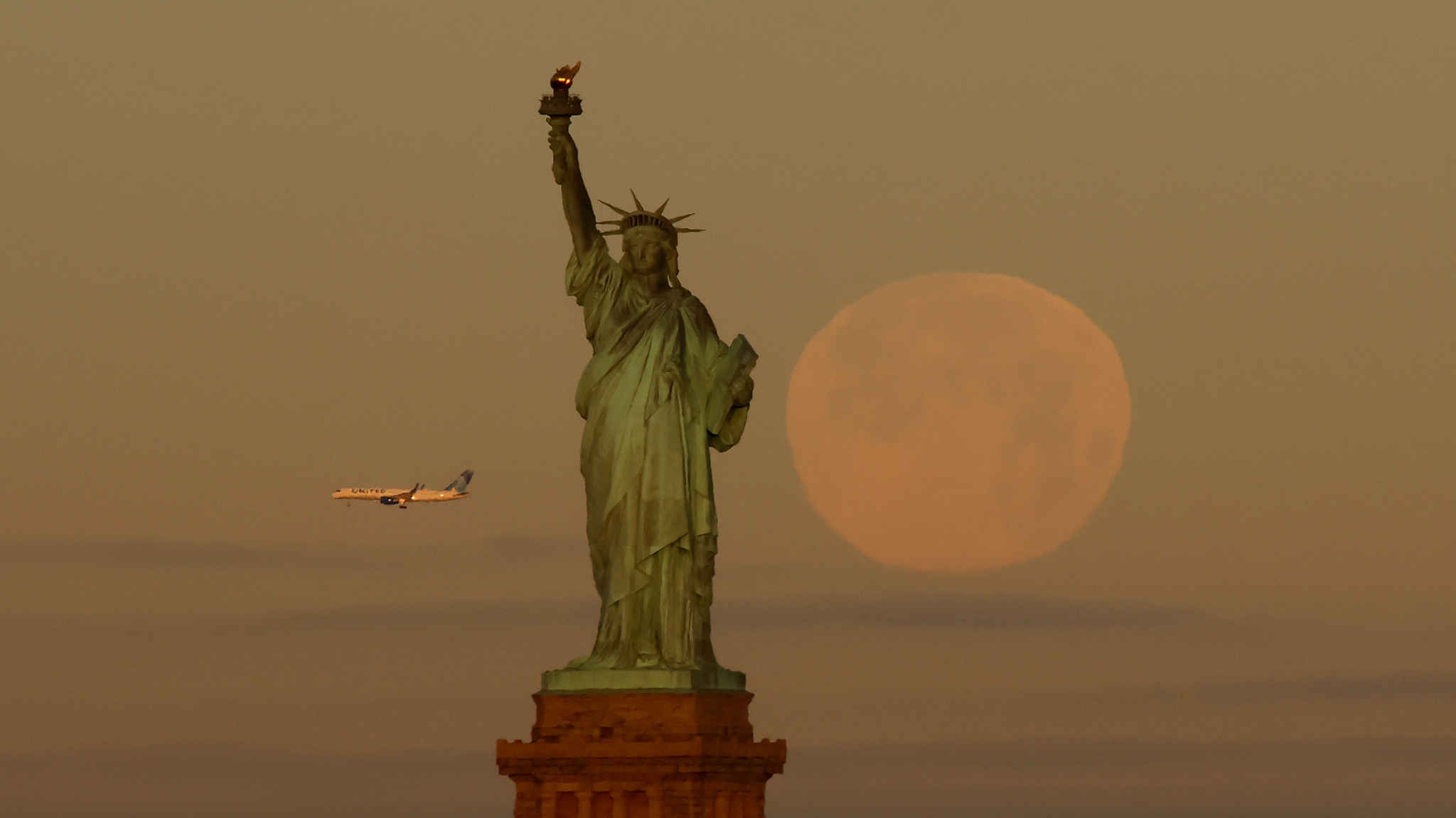 The full moon sets behind the Statue of Liberty as a United Airlines airplane flies past, New York City, the U.S., January 3, 2026. /CFP