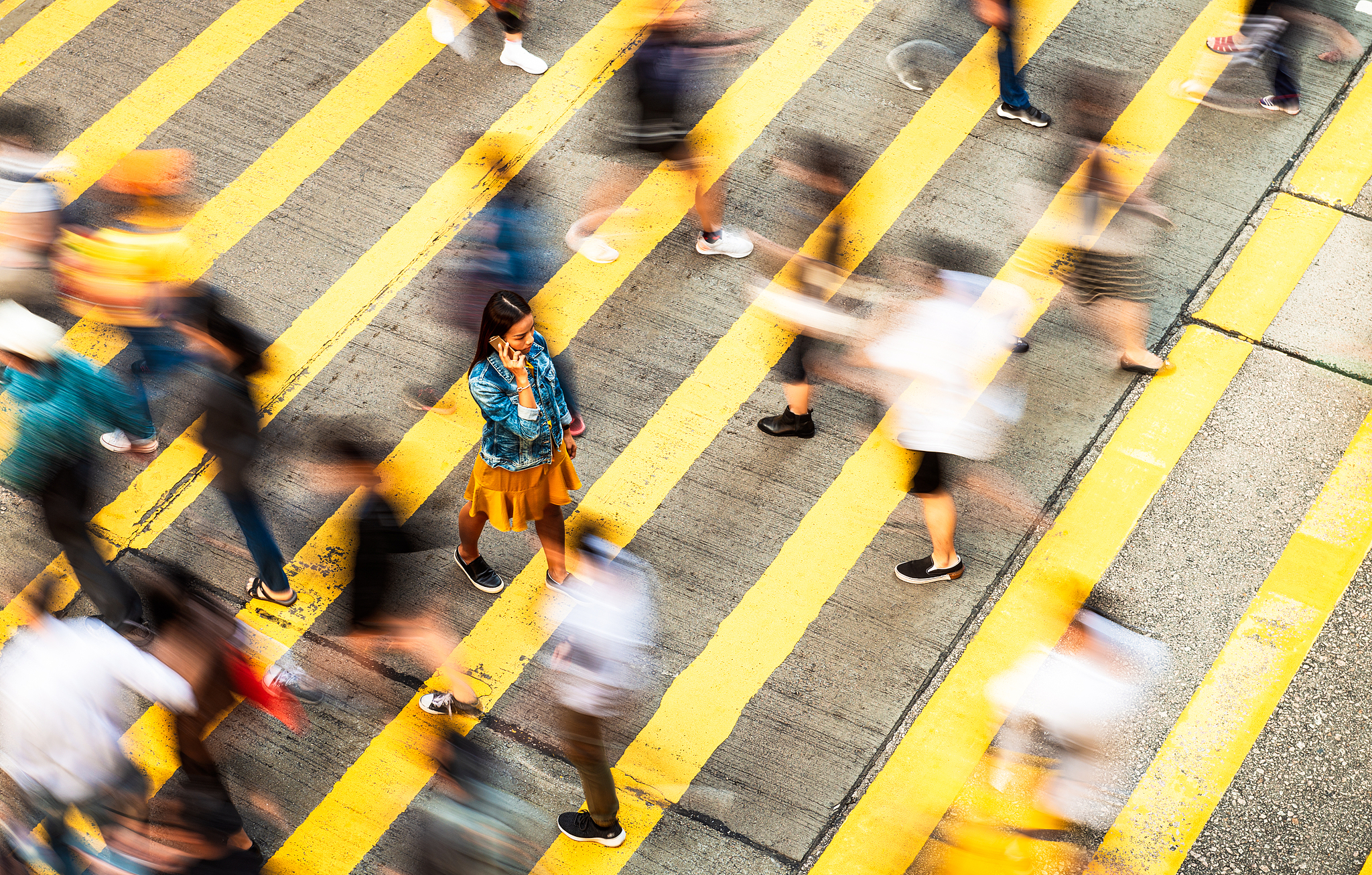 A woman stands out amid a blur of pedestrians crossing a busy street, captured with a slow-shutter effect. /VCG
