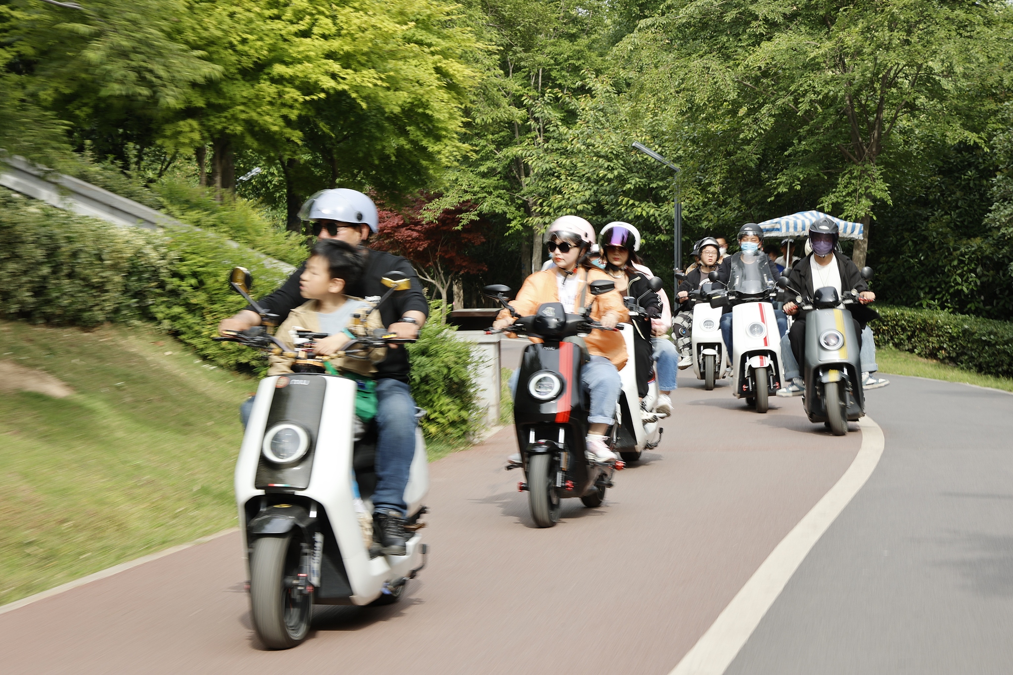Outdoor group ride of electric scooters, including a child passenger on the lead bike. /VCG