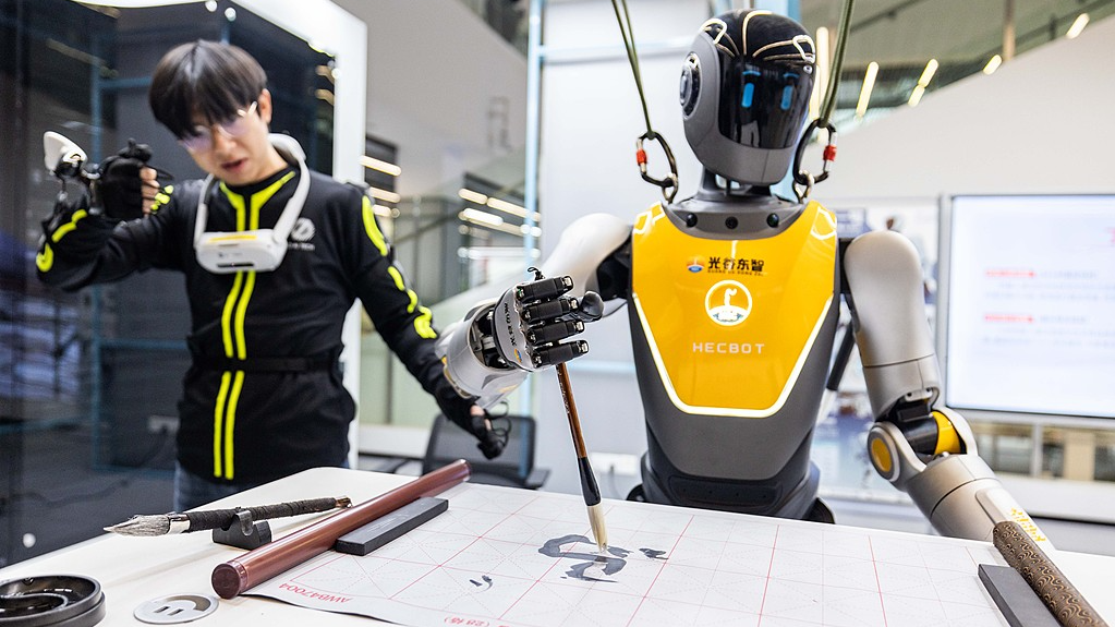 A trainer uses motion-capture technology to guide a humanoid robot through calligraphy practice at a store in Wuhan on January 19, 2026. /VCG