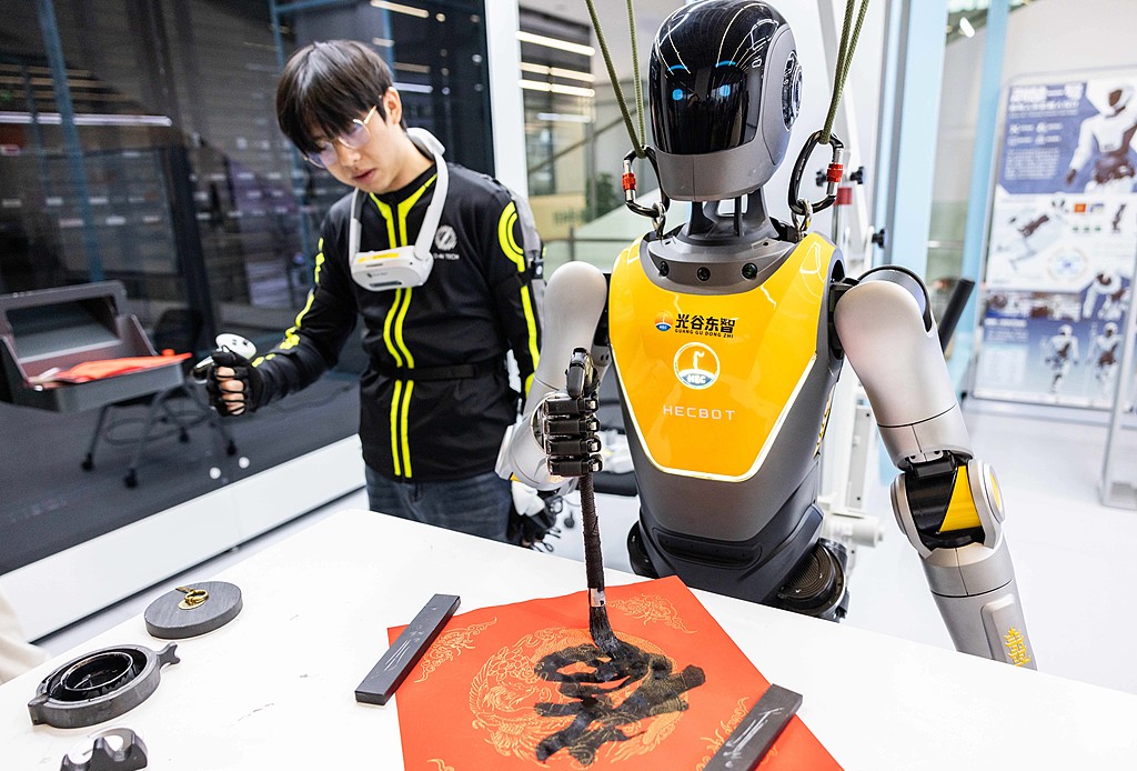 A trainer uses motion-capture technology to guide a humanoid robot through calligraphy practice at the humanoid robot 7S store in Wuhan on January 19, 2026. /VCG