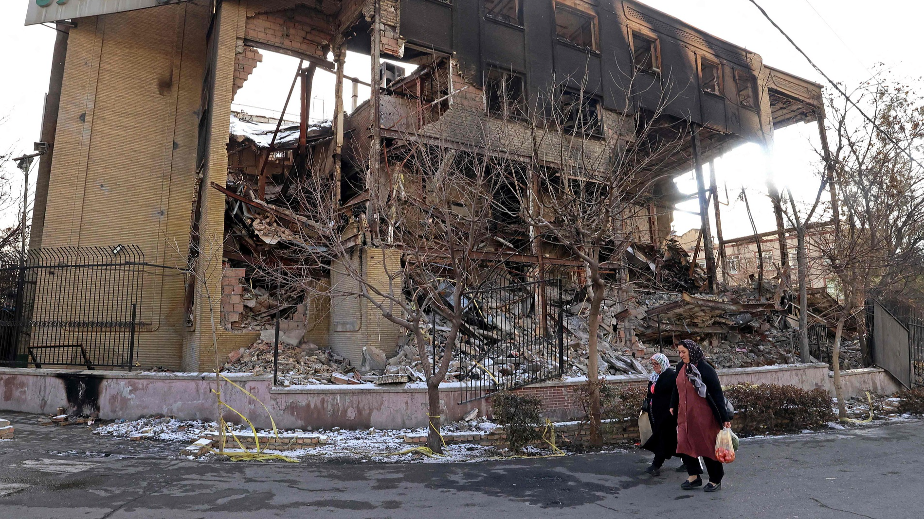 This photo taken during a tour for foreign media shows women walking past a government building that was burnt during recent public protests, in Tehran, Iran, on January 21, 2026. /VCG