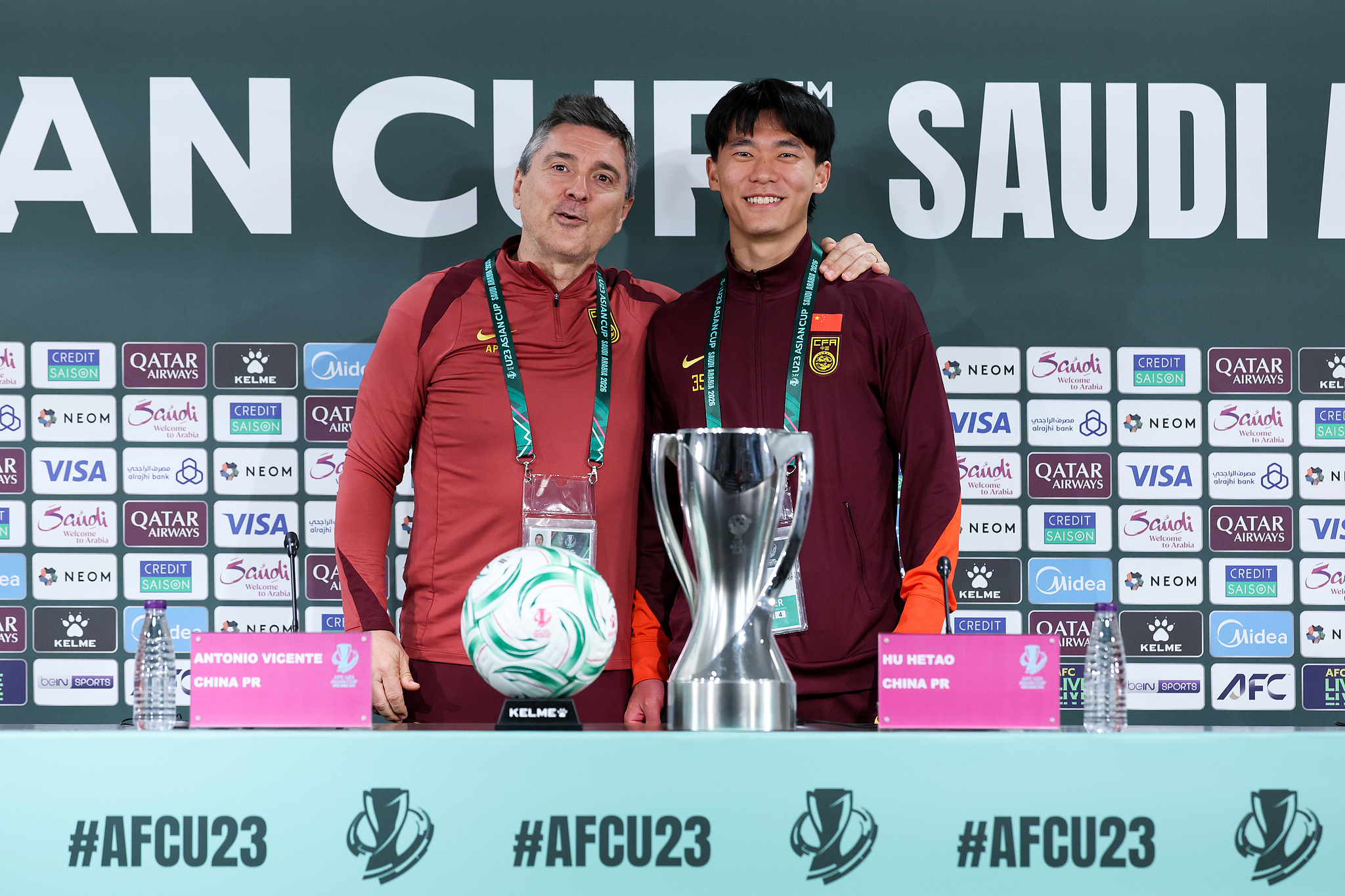 China coach Antonio Puche (L) and defender Hu Hetao pose behind the official game ball and championship trophy during a press conference on the eve of the AFC U23 Asian Cup final against Japan in Jeddah, Saudi Arabia, January 23, 2026. /VCG