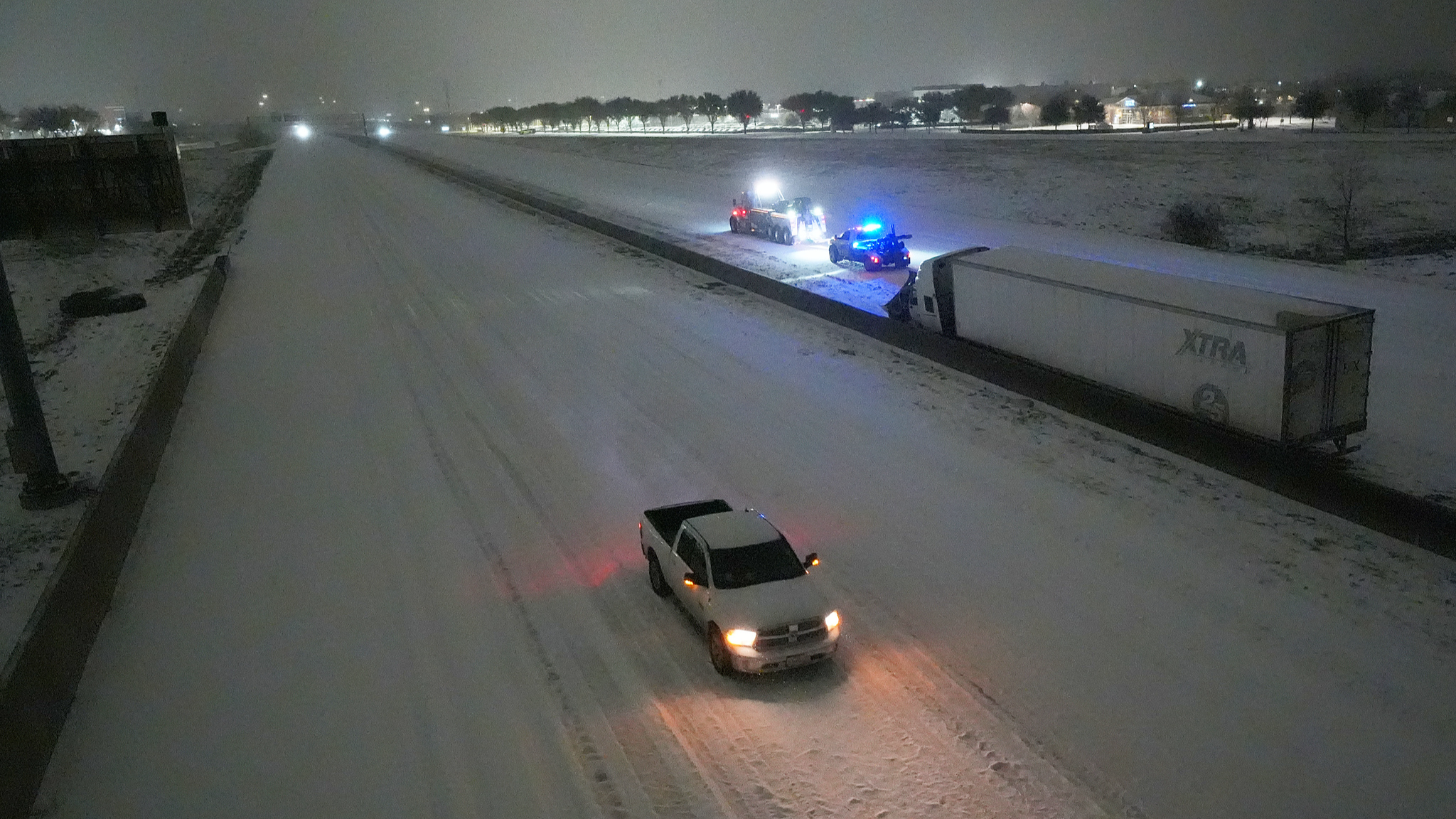 A pickup moves westbound on Interstate-20 as tow trucks, back, prepare to pull a disabled tractor trailer on the eastbound lanes during a snowstorm, January 25, 2026, in Arlington, Texas, U.S. /VCG