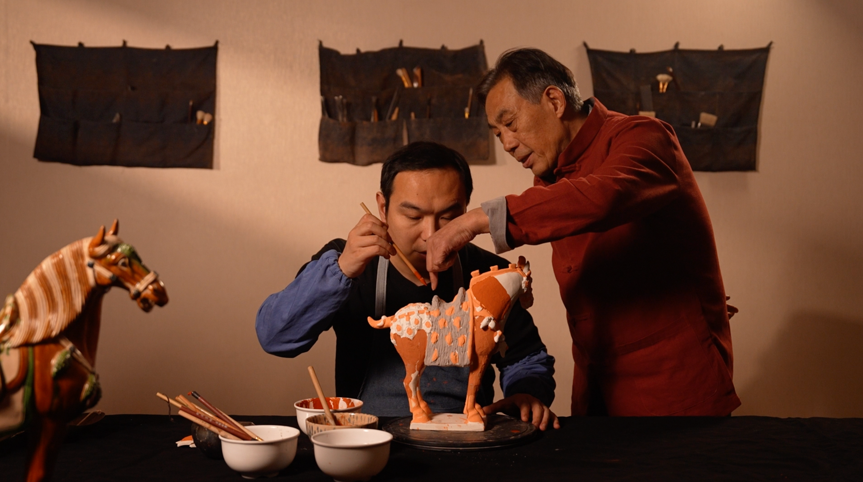 Gao Shuiwang instructs his son, Gao Zhe, on how to glaze pottery. /CGTN