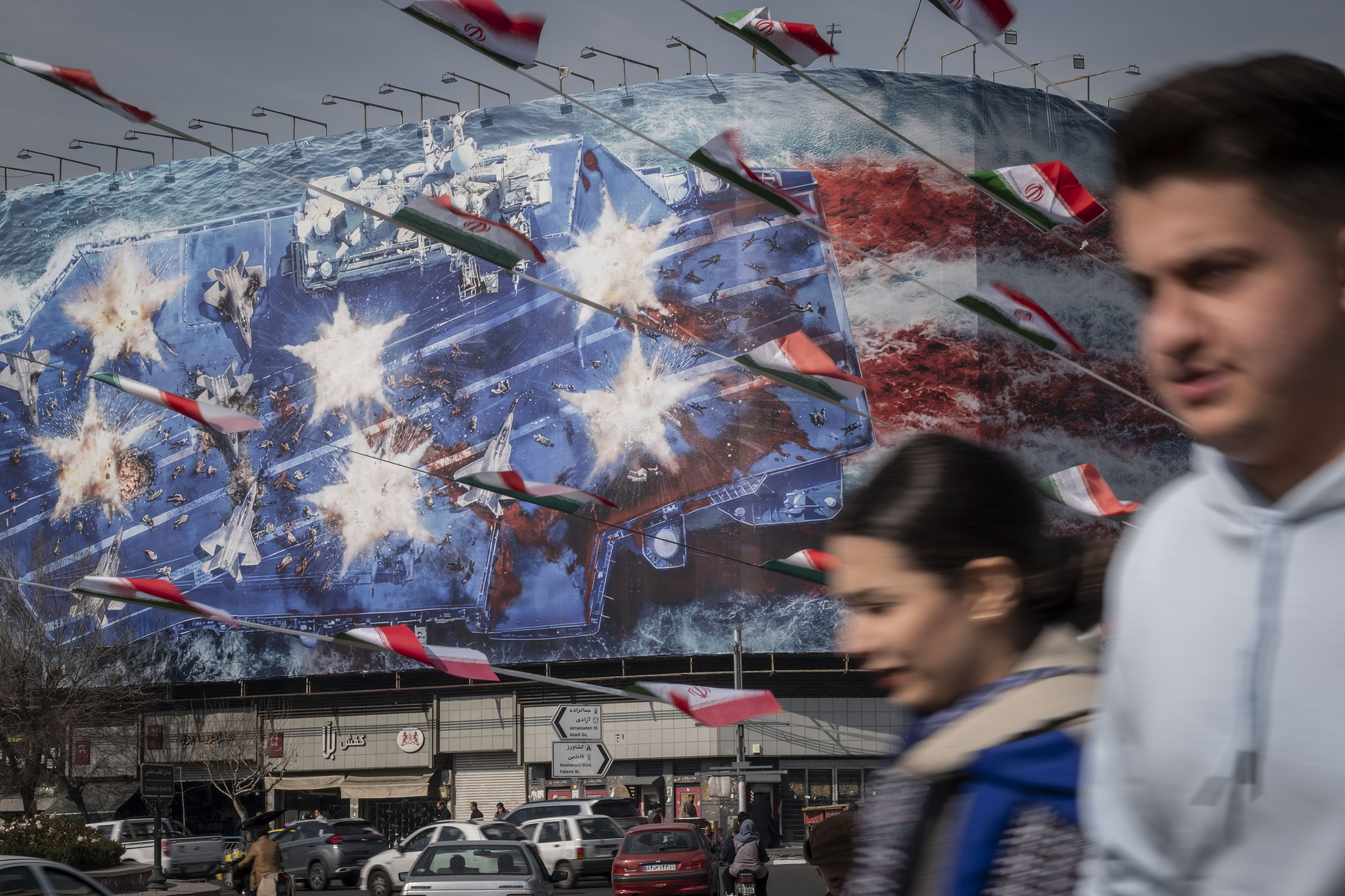 Iranian youths walk past a state building covered with a giant anti-U.S. billboard depicting a symbolic image of the destroyed USS Abraham Lincoln (CVN-72) aircraft carrier in downtown Tehran, Iran, on January 28, 2026. /VCG