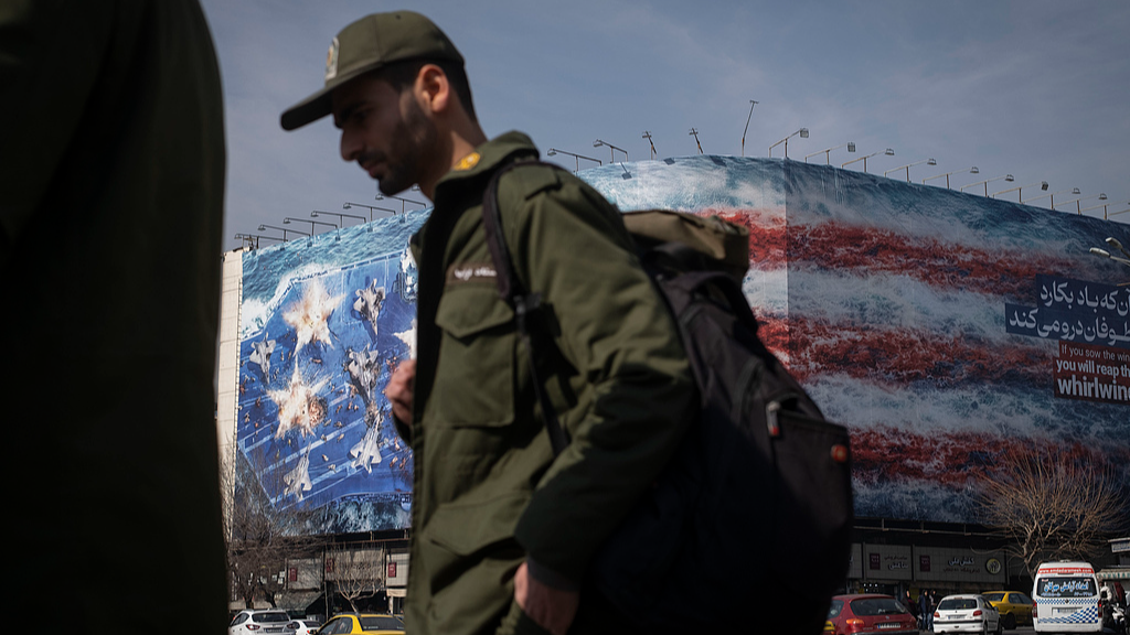 An Iranian soldier walks past a state building covered with a giant anti-U.S. billboard depicting a symbolic image of the destroyed USS Abraham Lincoln (CVN-72) aircraft carrier in downtown Tehran, Iran, January 28, 2026. /VCG