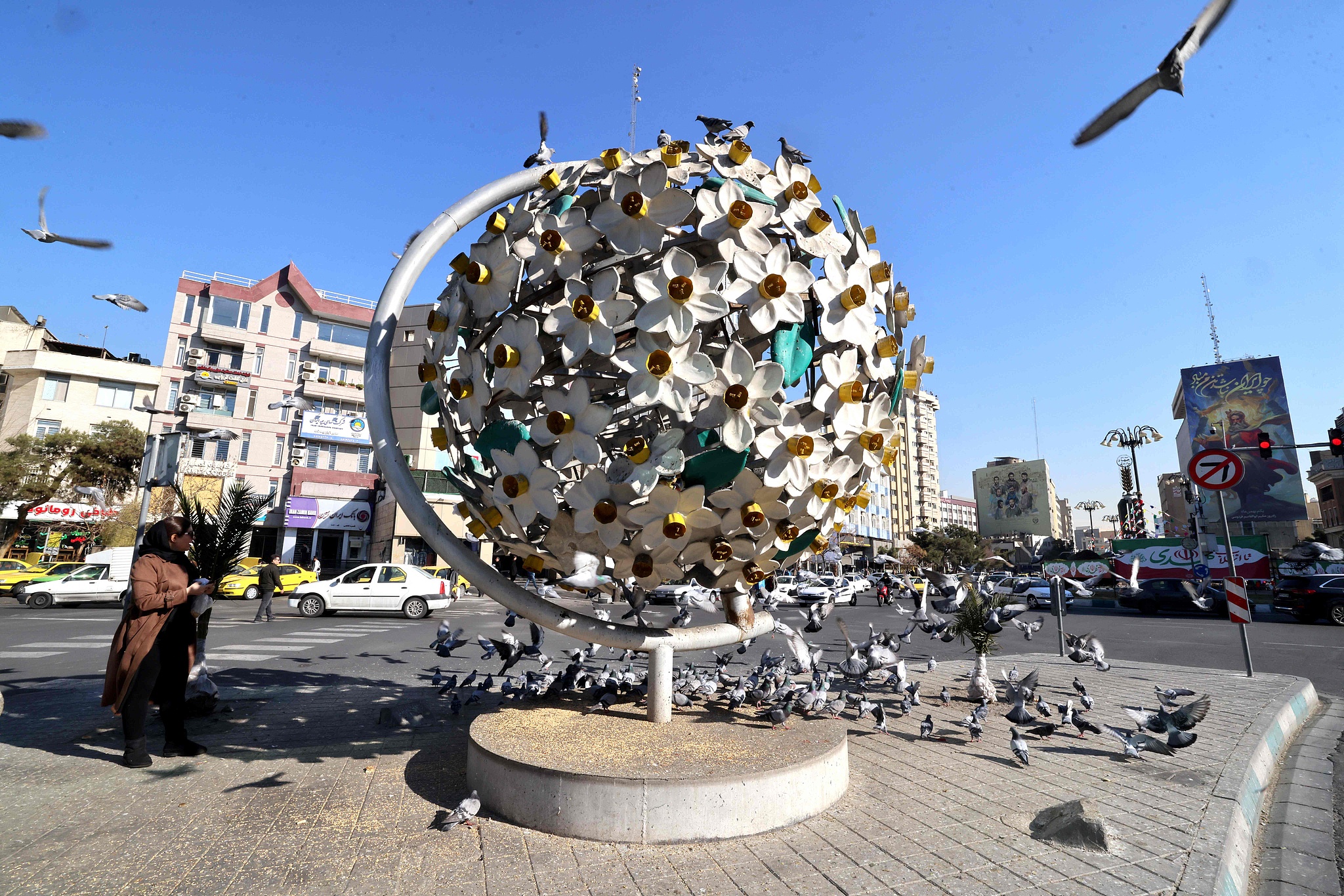 An Iranian woman walks past pigeons gathered at the foot of a sculpture in the Iranian capital Tehran on January 31, 2026./ VCG