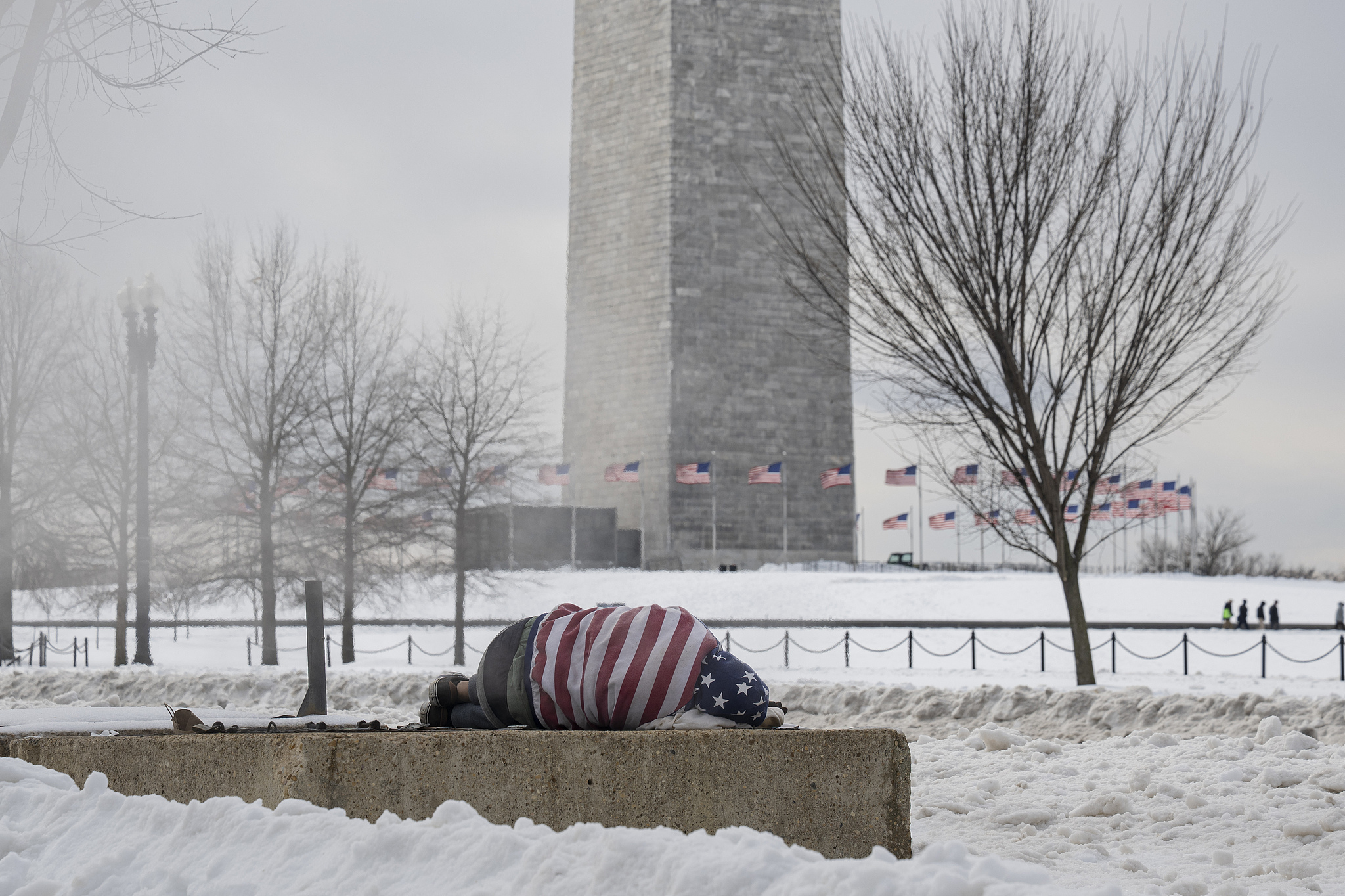 A homeless person sleeps on a warm air vent to keep warm after a heavy winter storm near the National Museum of African American History and Culture in Washington, DC, US, January 26, 2026. /VCG