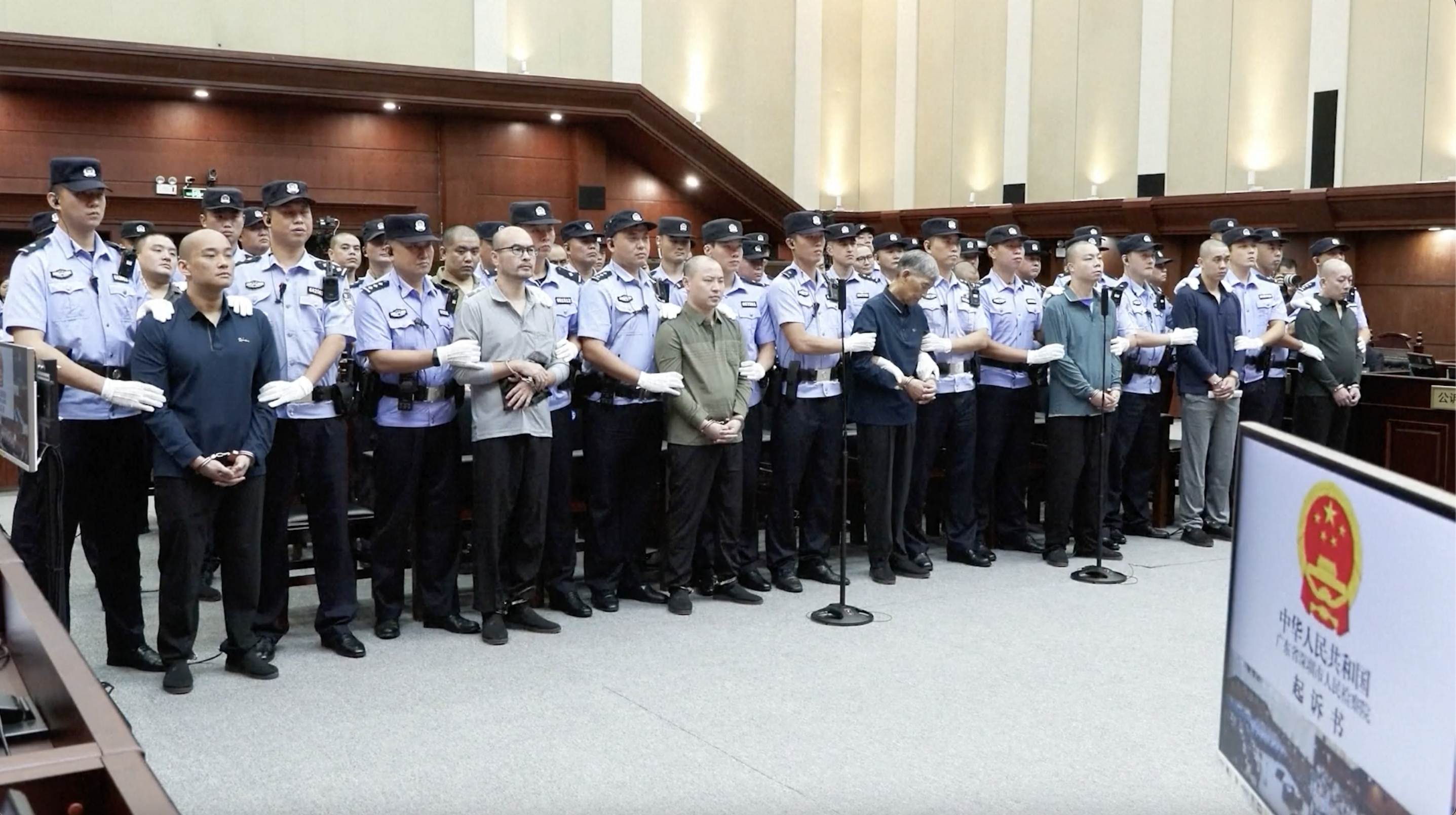 Defendants from the Bai family criminal group stand under police escort during court proceedings. /CMG