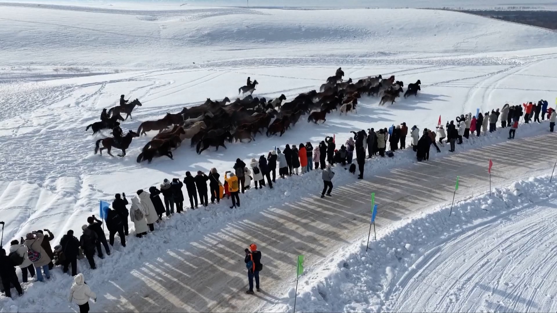 Tourists watch and take photos from the sidelines as herdsmen drive horses across the winter landscape. /CMG