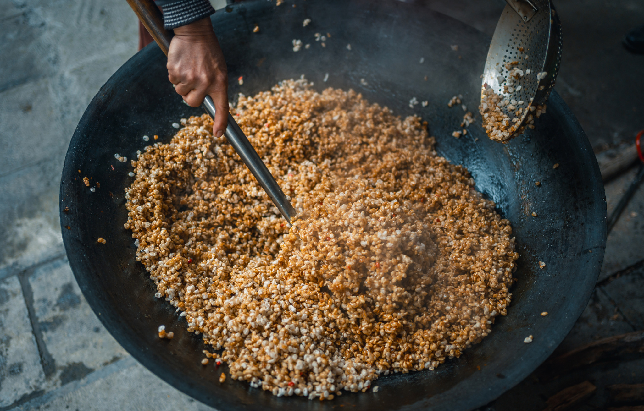 People of the Buyi ethnic group stir ingredients used to make brown sugar rice puffs in Wangmo County, Guizhou Province on February 11, 2026. /VCG