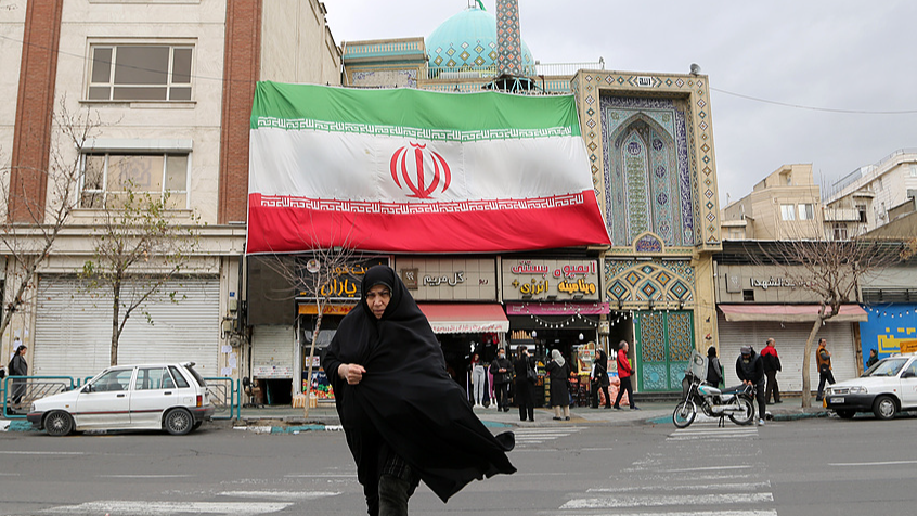 A woman crosses the road with an Iran flag seen behind in Tehran, Iran, February 9, 2026. /VCG