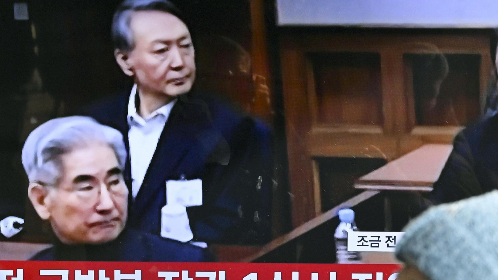 A television monitor at Seoul Station shows Yoon Suk-yeol (back, L) during sentencing in his insurrection case, Seoul Central District Court, February 19, 2026. /VCG