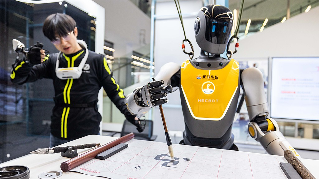 A robot trainer controls a humanoid robot to write. /VCG