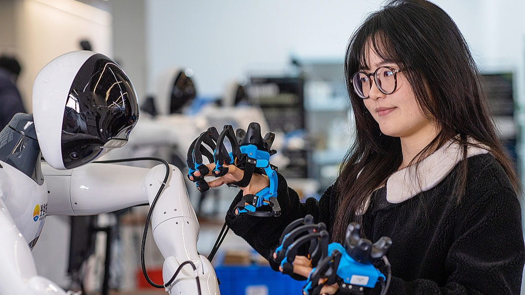 A robot trainer controls a humanoid robot to perform tasks. /VCG
