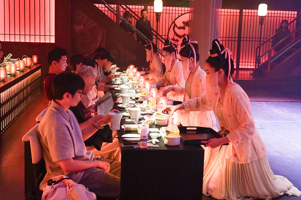 Staff dressed in Song Dynasty attire serve dishes at the Qingming Riverside Landscape Garden in Kaifeng, Henan Province, on September 26, 2025. /VCG