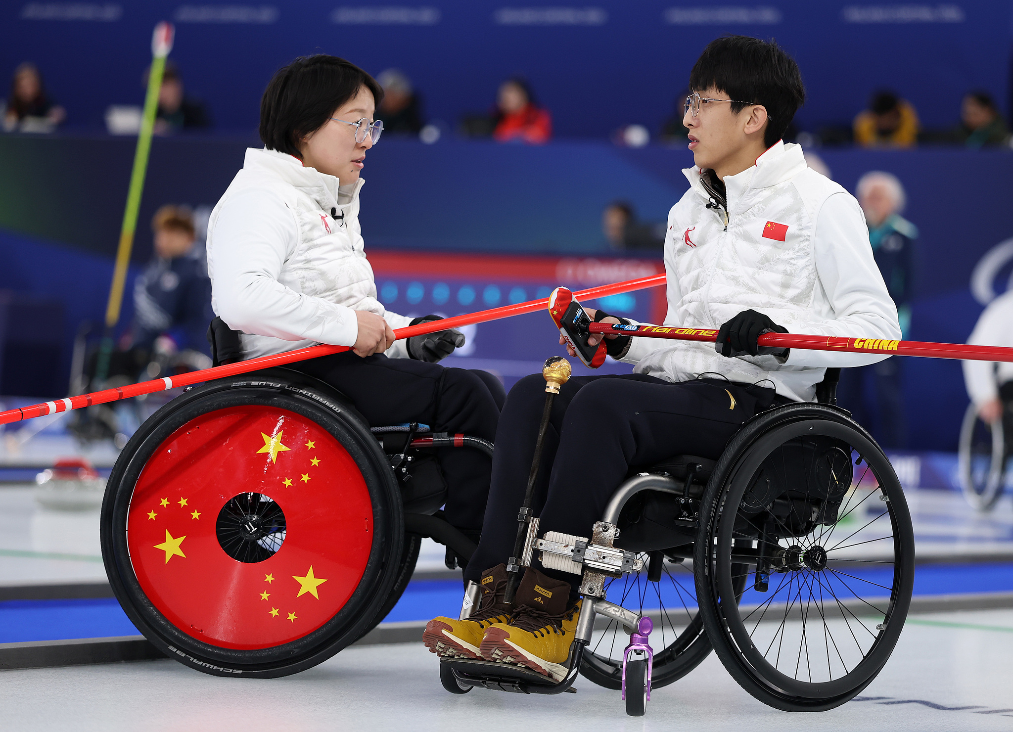Wang Meng (L) and Yang Jinqiao of China discuss strategy during an early wheelchair curling mixed doubles round robin contest against Italy at the 2026 Milano Cortina Winter Paralympics in Cortina d'Ampezzo, Italy, March 5, 2026. /VCG