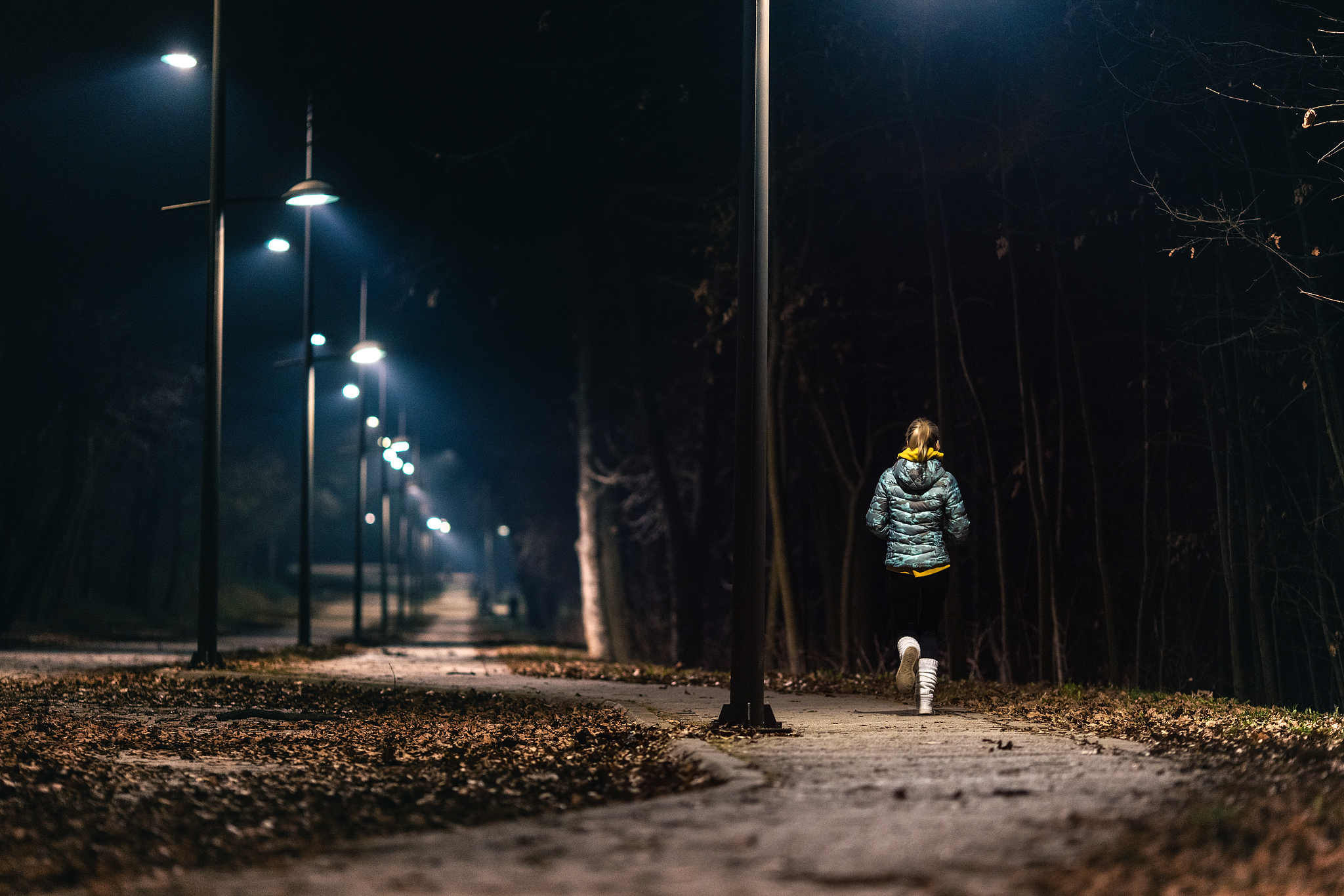 A woman runs along a well-lit pathway at night. /VCG