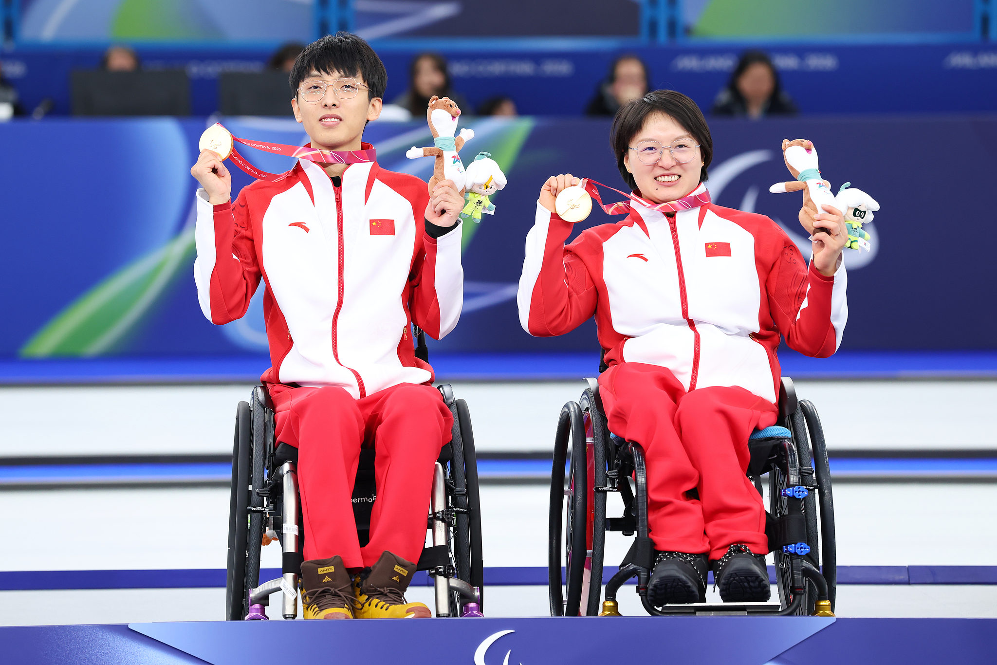 Gold medalists Yang Jinqiao (L) and Wang Meng display their awards after winning the mixed doubles wheelchair curling final at the 2026 Milano Cortina Winter Paralympics in Cortina d'Ampezzo, Italy, March 11, 2026. /VCG
