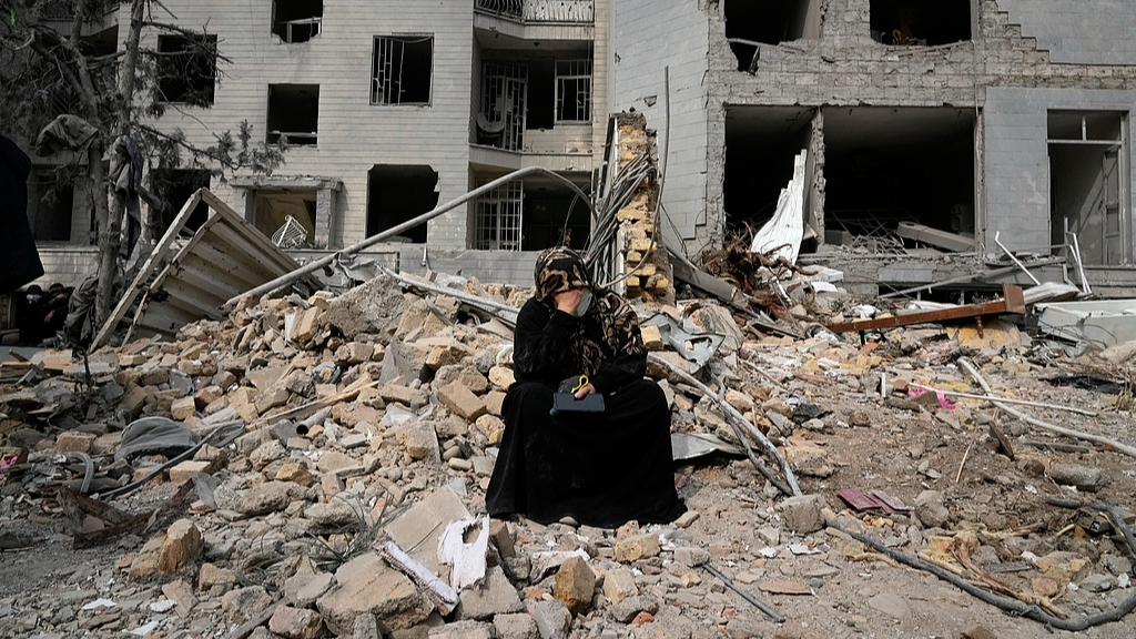 A woman sits on rubble across from a residential building damaged during the US-Israeli attacks in Tehran, Iran, March 12, 2026. /VCG