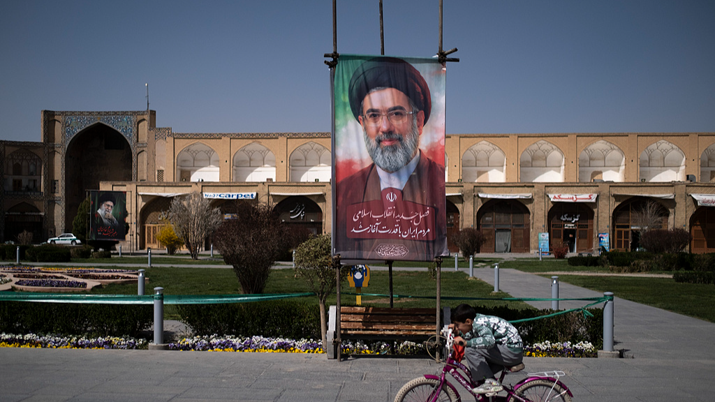 A young Iranian boy rides a bicycle past a portrait of Iran's Supreme Leader Ayatollah Mojtaba Khamenei in the historic Naqsh-e Jahan Square in Isfahan, Iran, March 11, 2026. /VCG