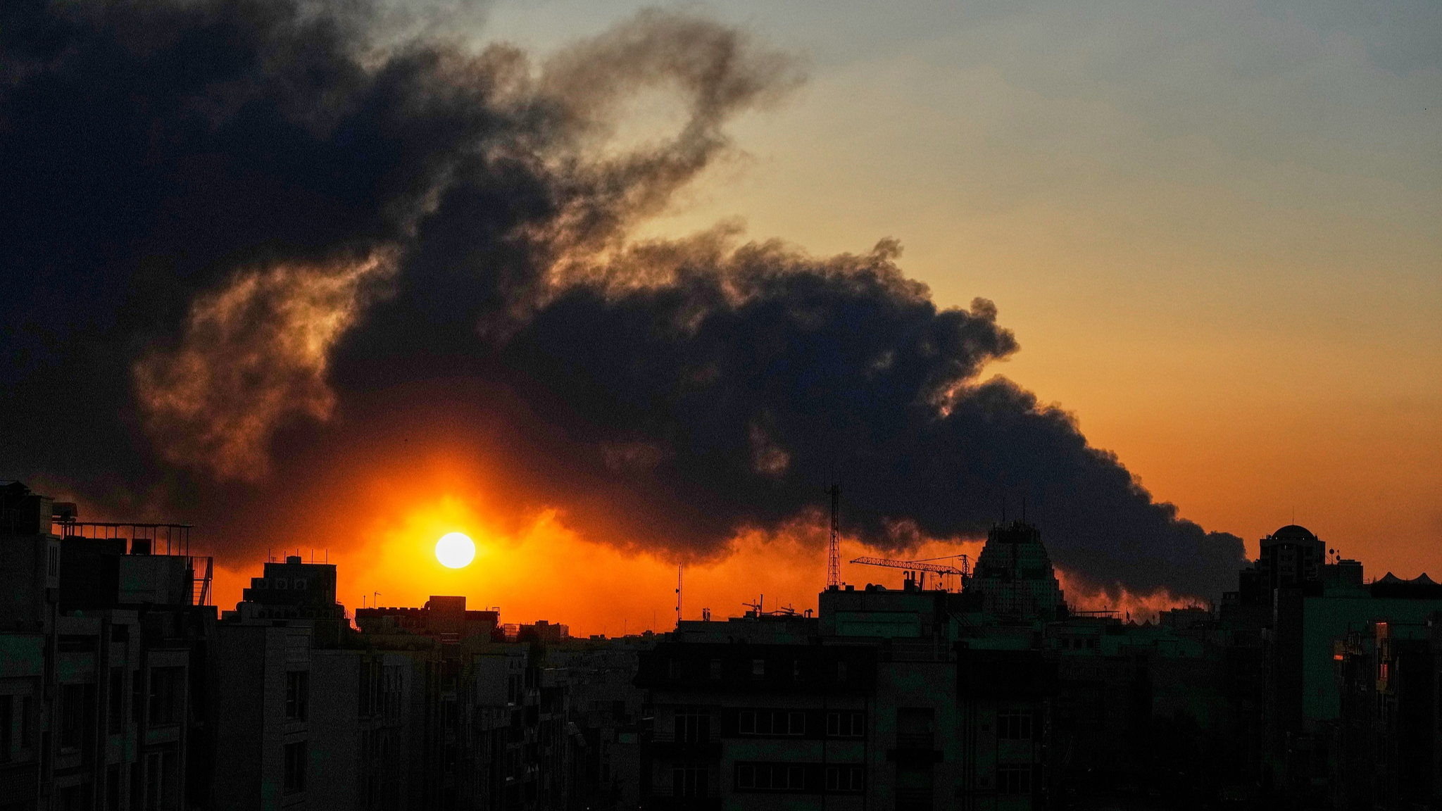The sun sets behind a plume of smoke rising from a US-Israeli military strike in Tehran, Iran, March 3, 2026. / CFP