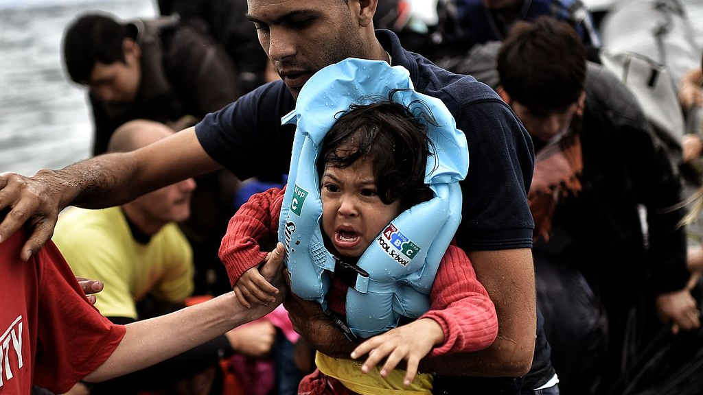 A man carries a child as refugees and migrants arrive on a dinghy to the island of Lesbos, Greece, September 30, 2015. /VCG