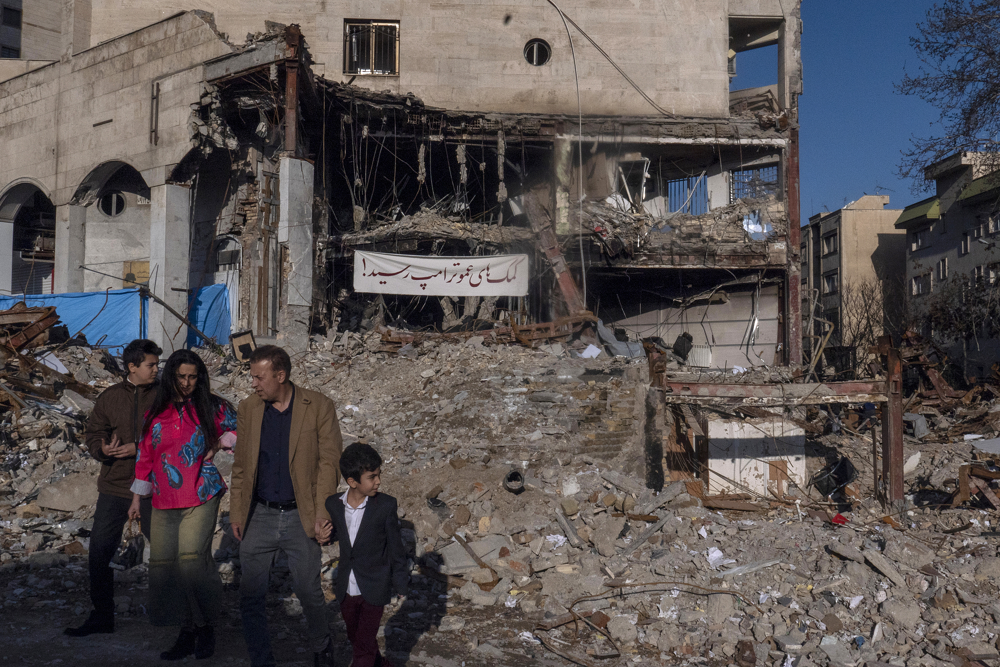 A family passes a devastated residential and commercial building in the Shahrak-e Gharb neighborhood of Tehran, Iran, March 21, 2026. /CFP