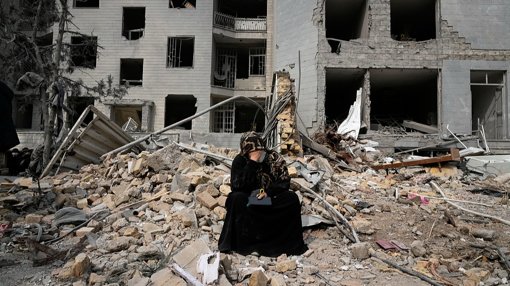A woman sits on rubble from a residential building damaged during the US-Israeli air campaign in Tehran, Iran, March 12, 2026. /VCG
