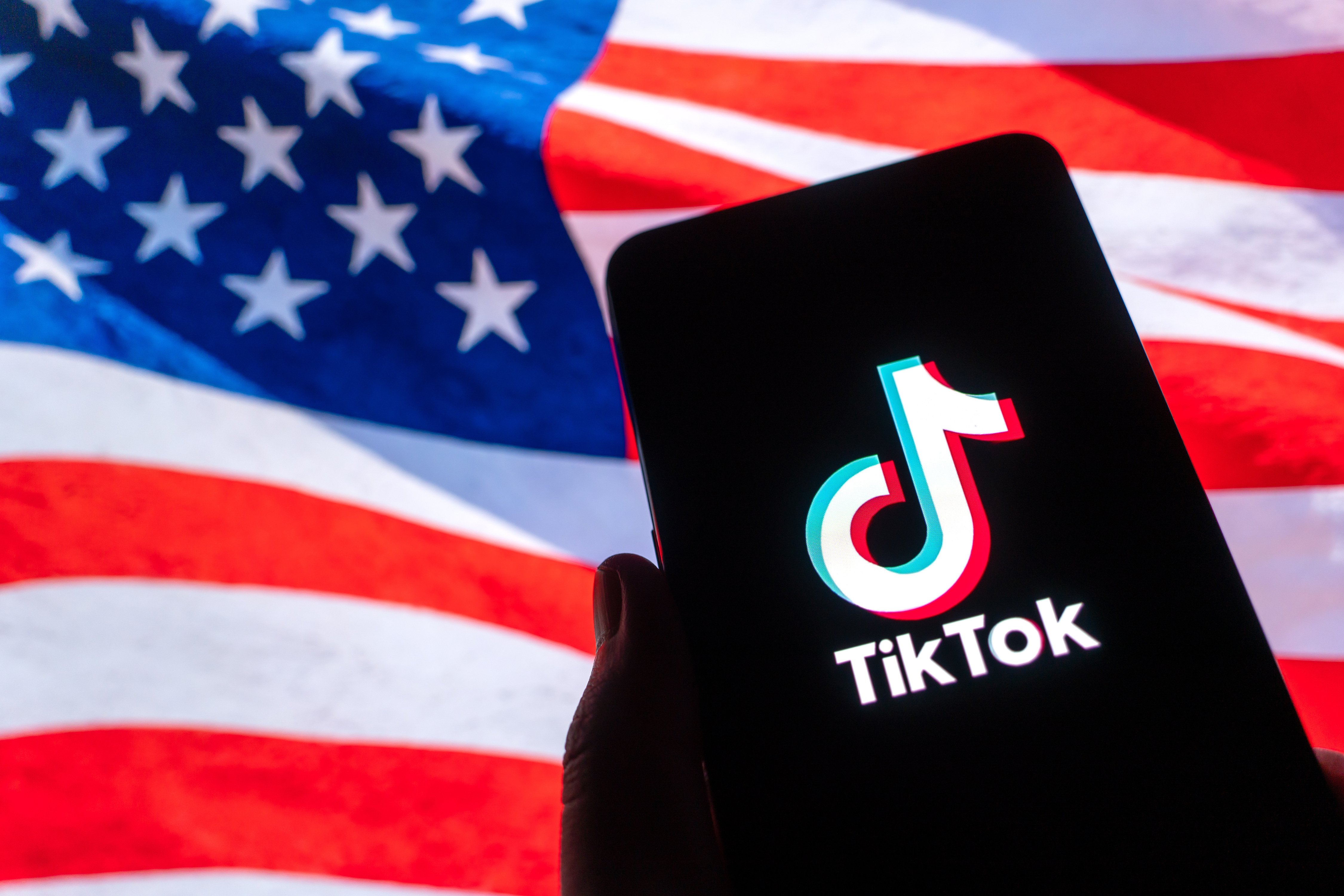The logo of TikTok is seen on a smartphone held in front of an American flag. /VCG