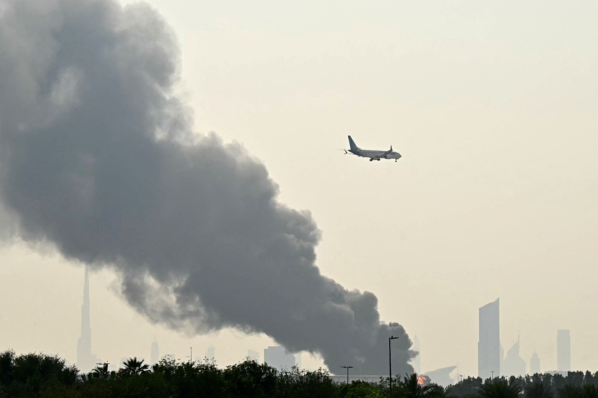 An Emirates aircraft flies past plumes of smoke from an ongoing fire near Dubai International Airport in Dubai on March 16, 2026. /VCG