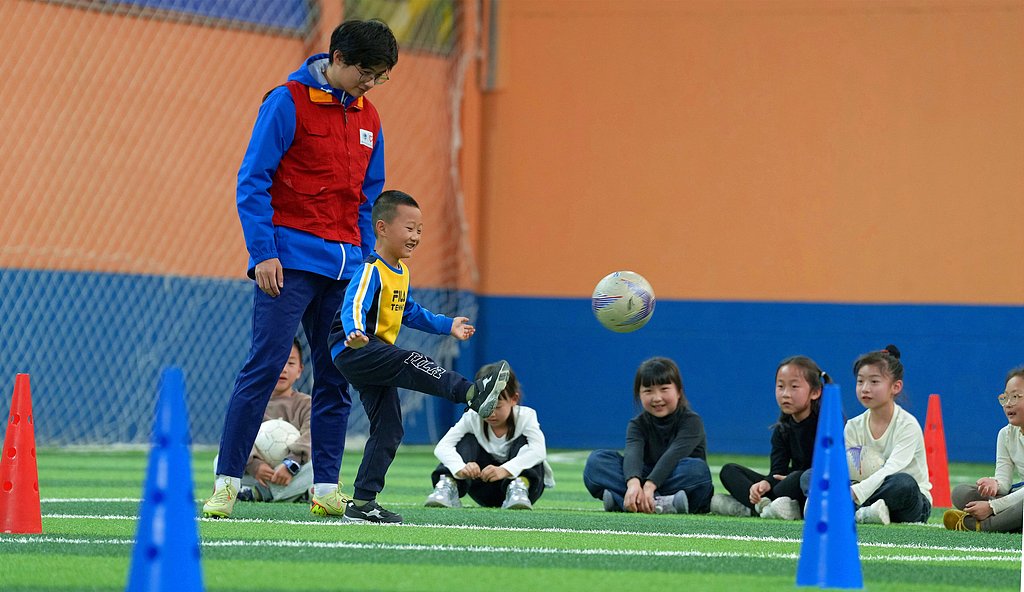 A volunteer trains children how to play football under supervised programs during their spring break in Haian, Jiangsu Province, China, April 2, 2026. /VCG
