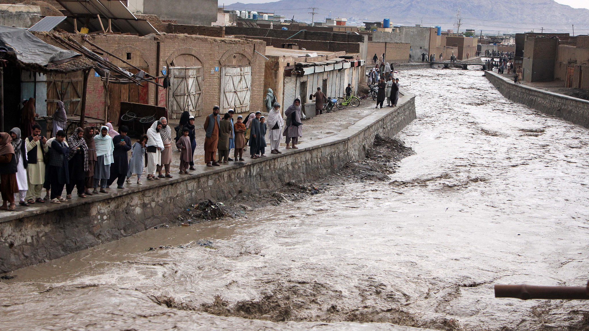 People gather as rainwater flows through a canal following heavy rains in Kandahar, Afghanistan, April 1, 2026. /VCG