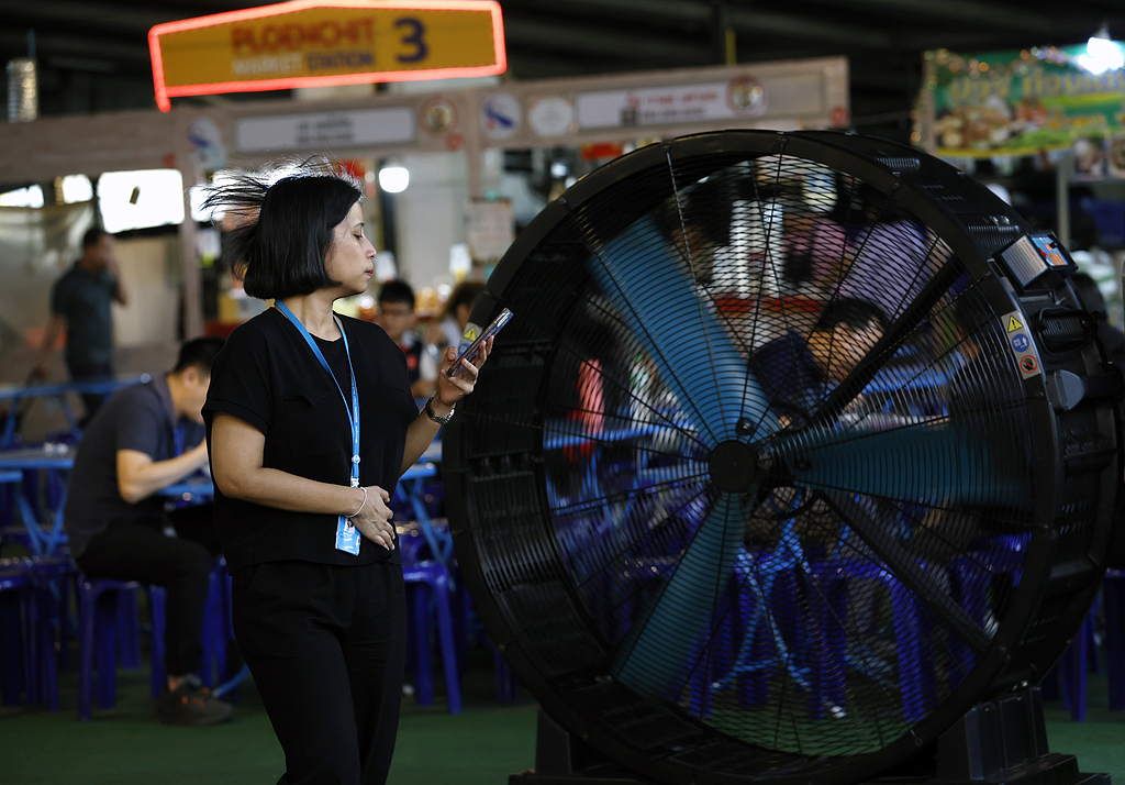A Thai woman uses a large fan to cool off at a street food court in Bangkok, Thailand, March 26, 2026. /CFP