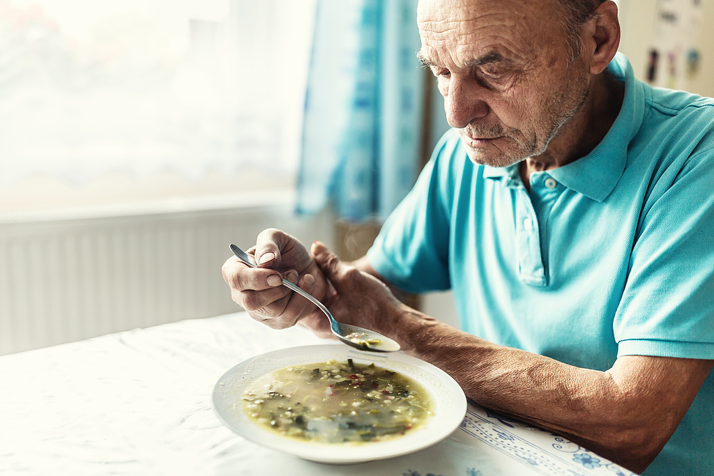 A man with Parkinson's disease supports his arm as he struggles to drink soup. /VCG
