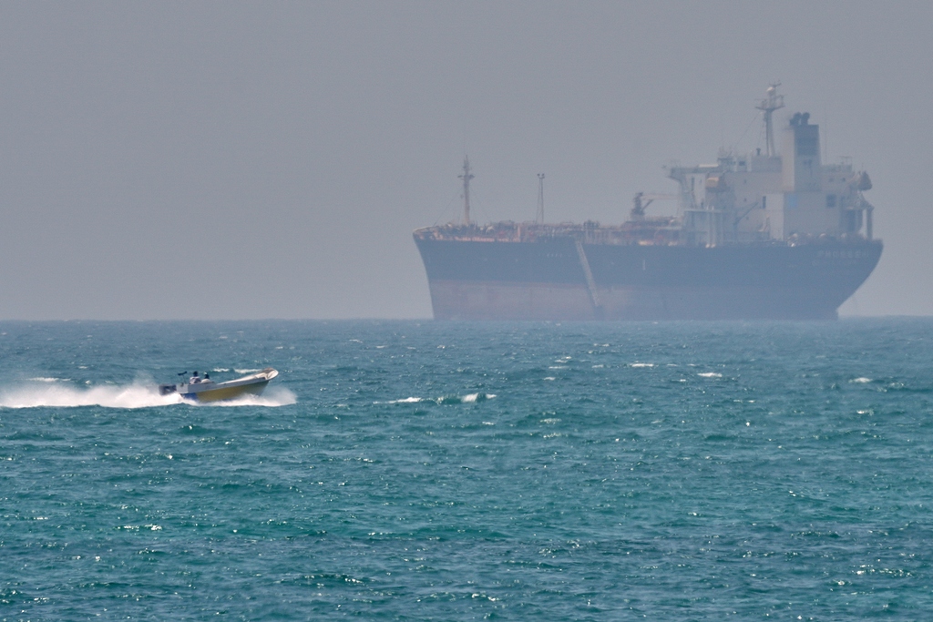 A boat sails past a tanker anchored on the Strait of Hormuz off the coast of Qeshm island, Iran, April 18, 2026./VCG