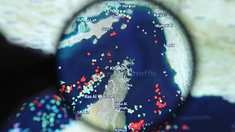 A laptop screen displays a map of the Strait of Hormuz alongside real-time vessel tracking data from Marine Traffic, with a magnifying glass highlighting the strategically vital waterway for oil shipments. /VCG