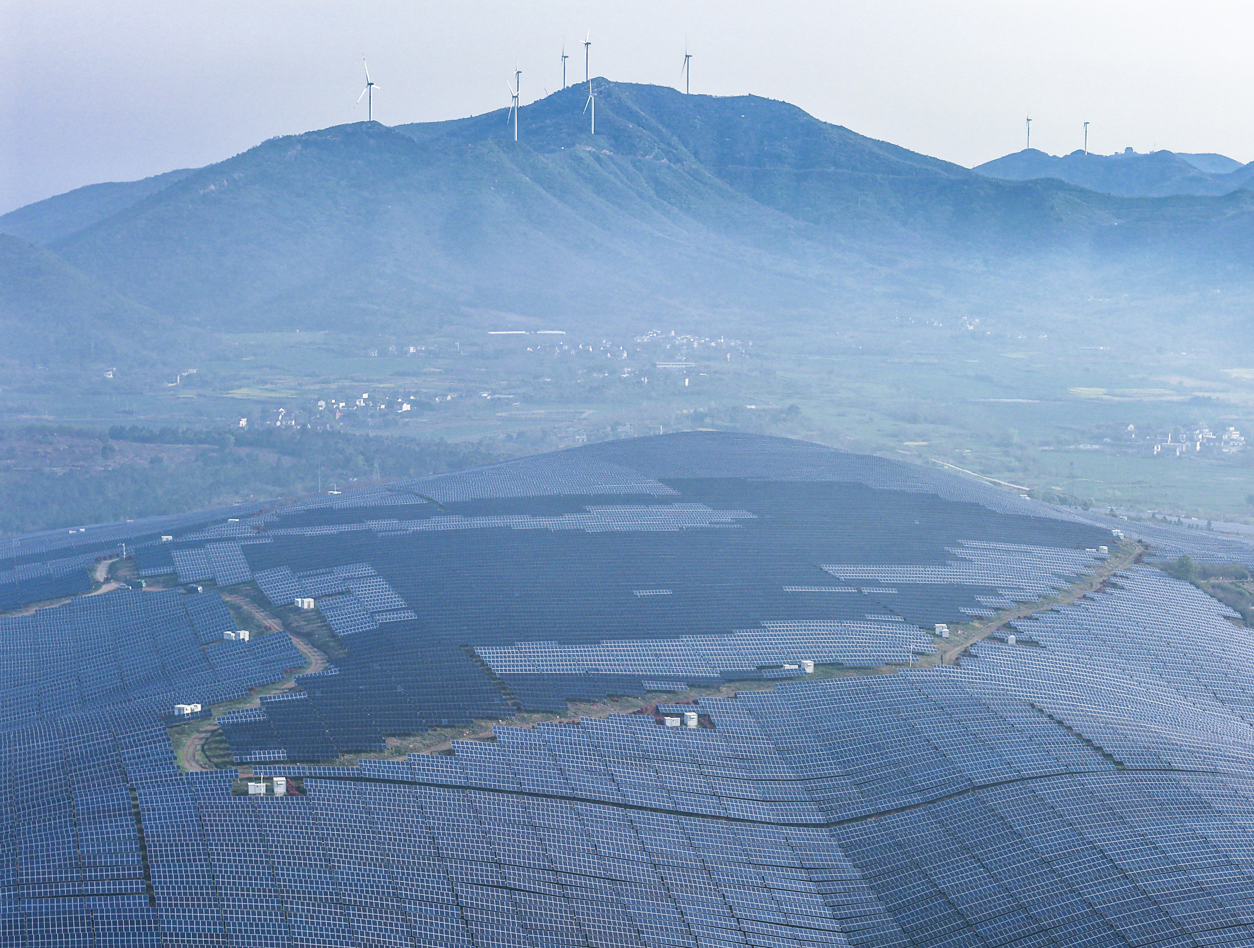 Arrays of solar panels at the Yanqiao Town photovoltaic power station, with wind turbines on the distant mountains, in Wuwei, Anhui Province, April 4, 2026. /VCG