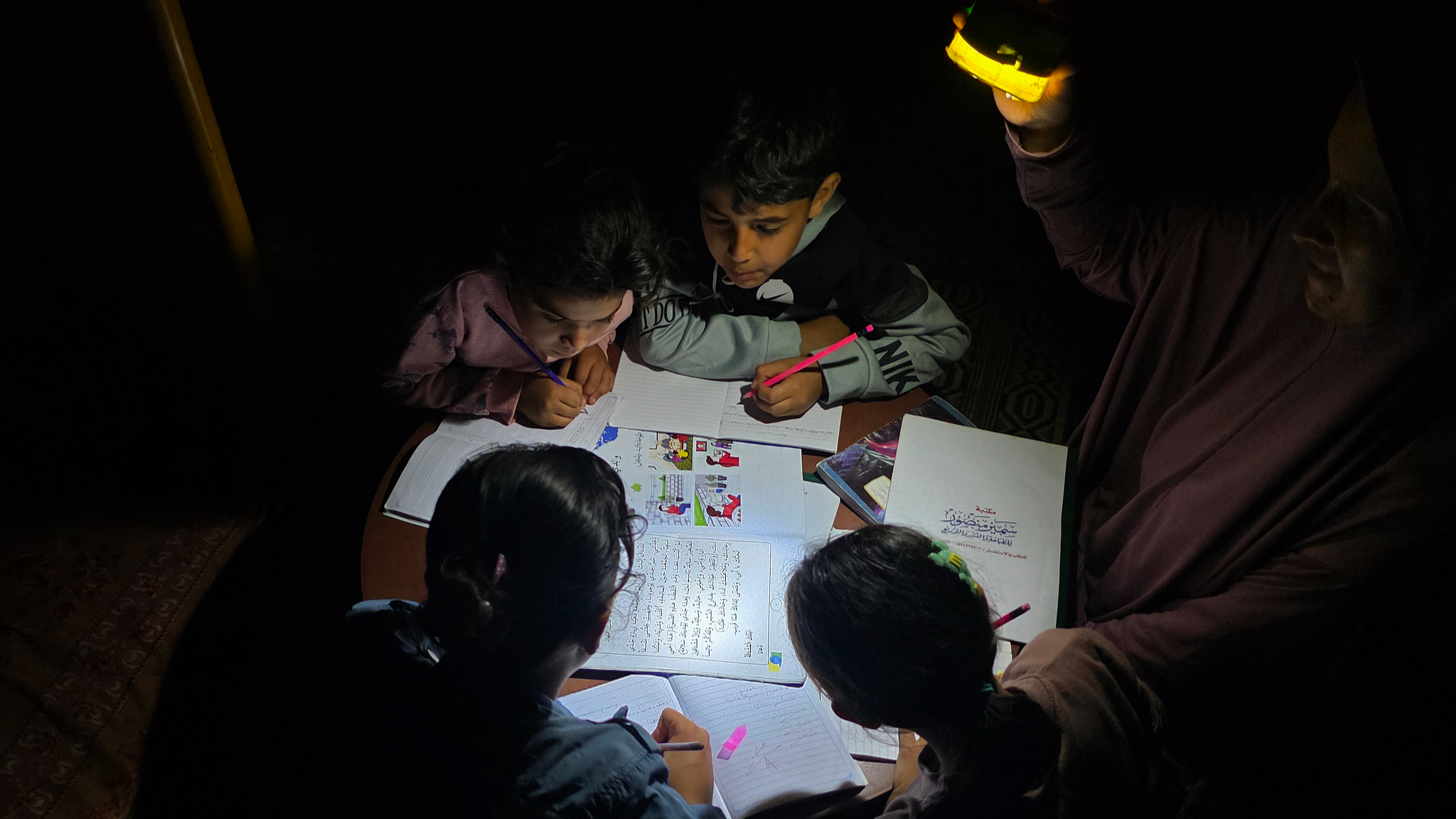 Palestinian mother Maysa Hamdi teaches her children and her nephews, who lost their mother, by the light of a lamp inside a tent in the Mawasi area of Khan Younis, southern Gaza Strip, on May 3, 2026. /VCG