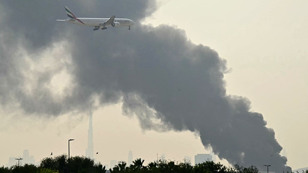 An Emirates aircraft flies past plumes of smoke from an ongoing fire near Dubai International Airport, Dubai, UAE, March 16, 2026. /VCG