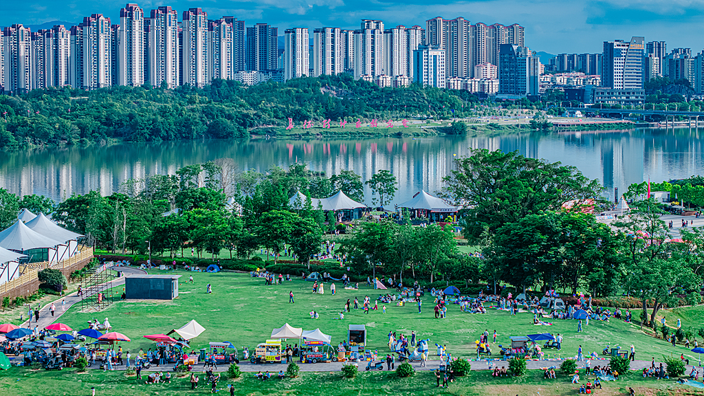 Crowds of visitors fill a city park, where lush trees and clear waters blend harmoniously with urban buildings, Ganzhou City, east China's Jiangxi Province, May 1, 2026. /VCG
