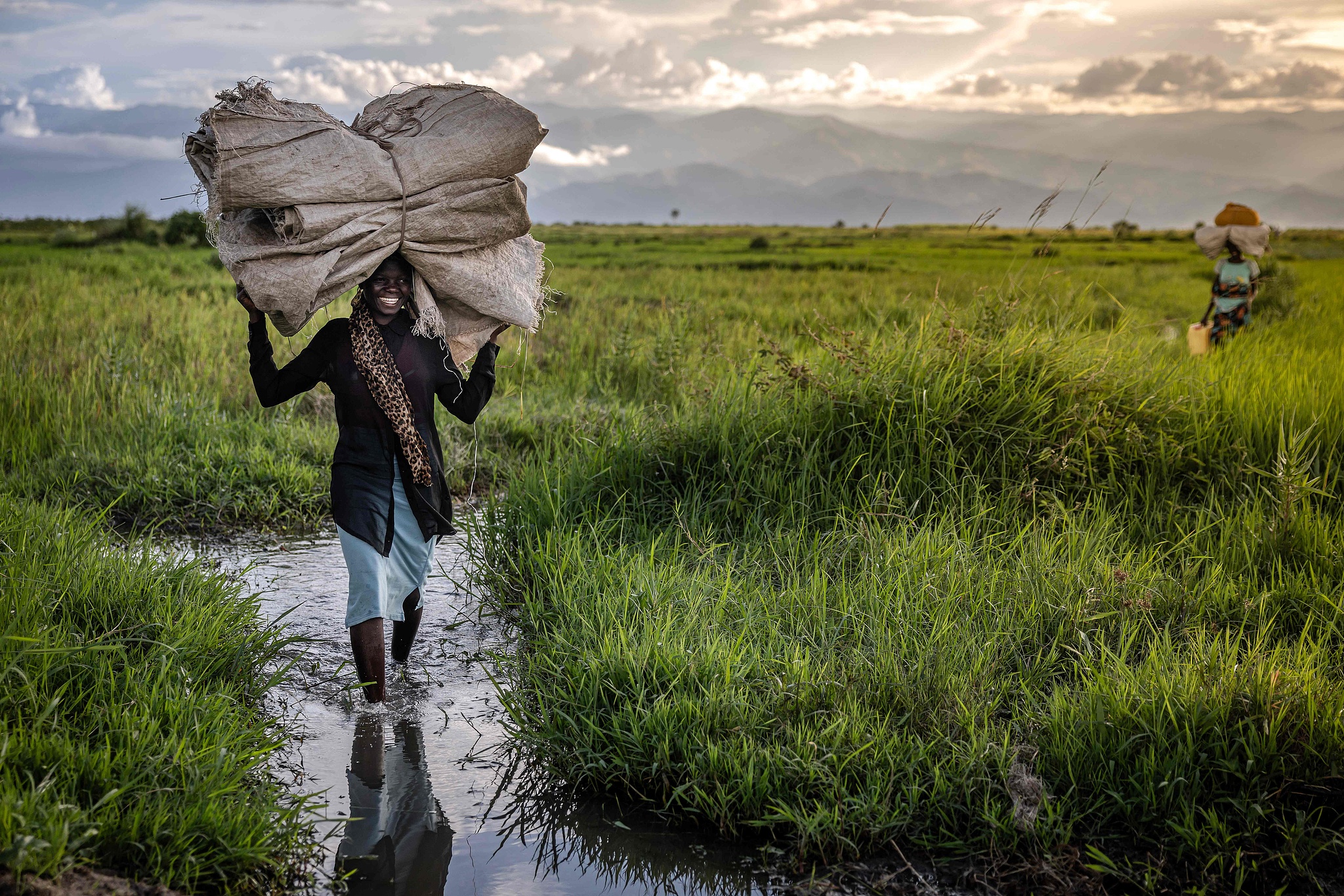 A farmer carries farming tools and a tarpaulin in rice fields on the outskirts of Bujumbura, Burundi, on May 8, 2025. /VCG