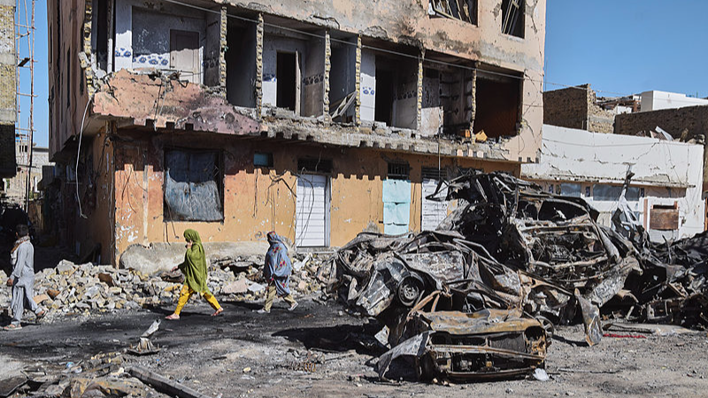 People walk past damaged cars and a building at the site of a bomb explosion near a railway track in Quetta, Balochistan Province, in southwestern Pakistan, May 25, 2026. /VCG