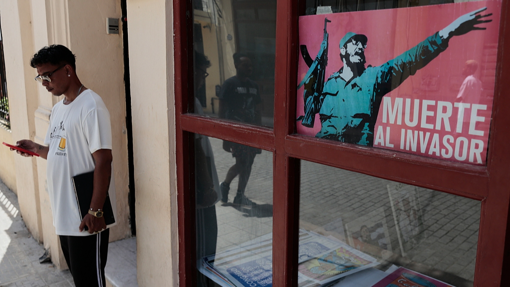 A man stands by an image of Fidel Castro, reading in Spanish, 