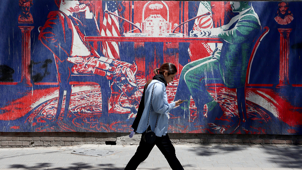 An Iranian girl walks next to a mural depicting Iran and US negotiations at a table, near the former US Embassy in Tehran, Iran, May 26, 2026. /VCG