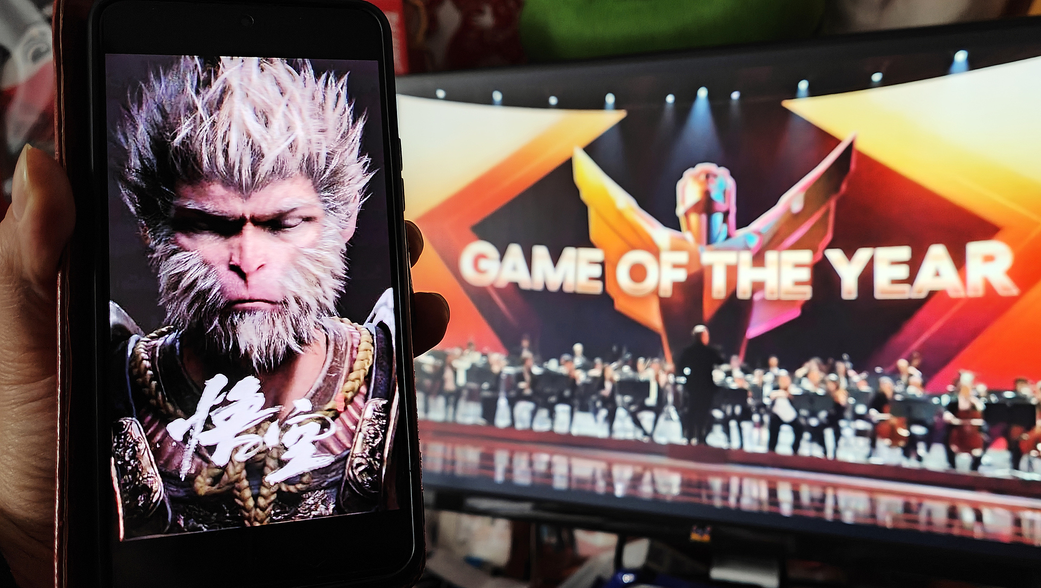A gamer in Shanghai holds up a phone displaying a Black Myth: Wukong poster while watching the game win the Game of the Year Award at The Game Awards (TGA) 2024 ceremony in December 2024. /VCG
